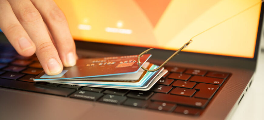 Ein Bild, das einen Menschen zeigt, der versucht, Phishing und Online-Betrug zu verhindern, indem er eine durchgesickerte Kreditkarte hält, die an einem Fischhaken über einer PC-Tastatur hängt.