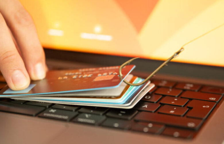 Ein Bild, das einen Menschen zeigt, der versucht, Phishing und Online-Betrug zu verhindern, indem er eine durchgesickerte Kreditkarte hält, die an einem Fischhaken über einer PC-Tastatur hängt.